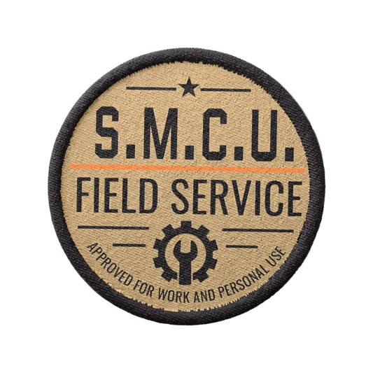 A circular embroidered patch with a black border, tan background, and black text reading 'S.M.C.U. Field Service Approved for work and personal use'